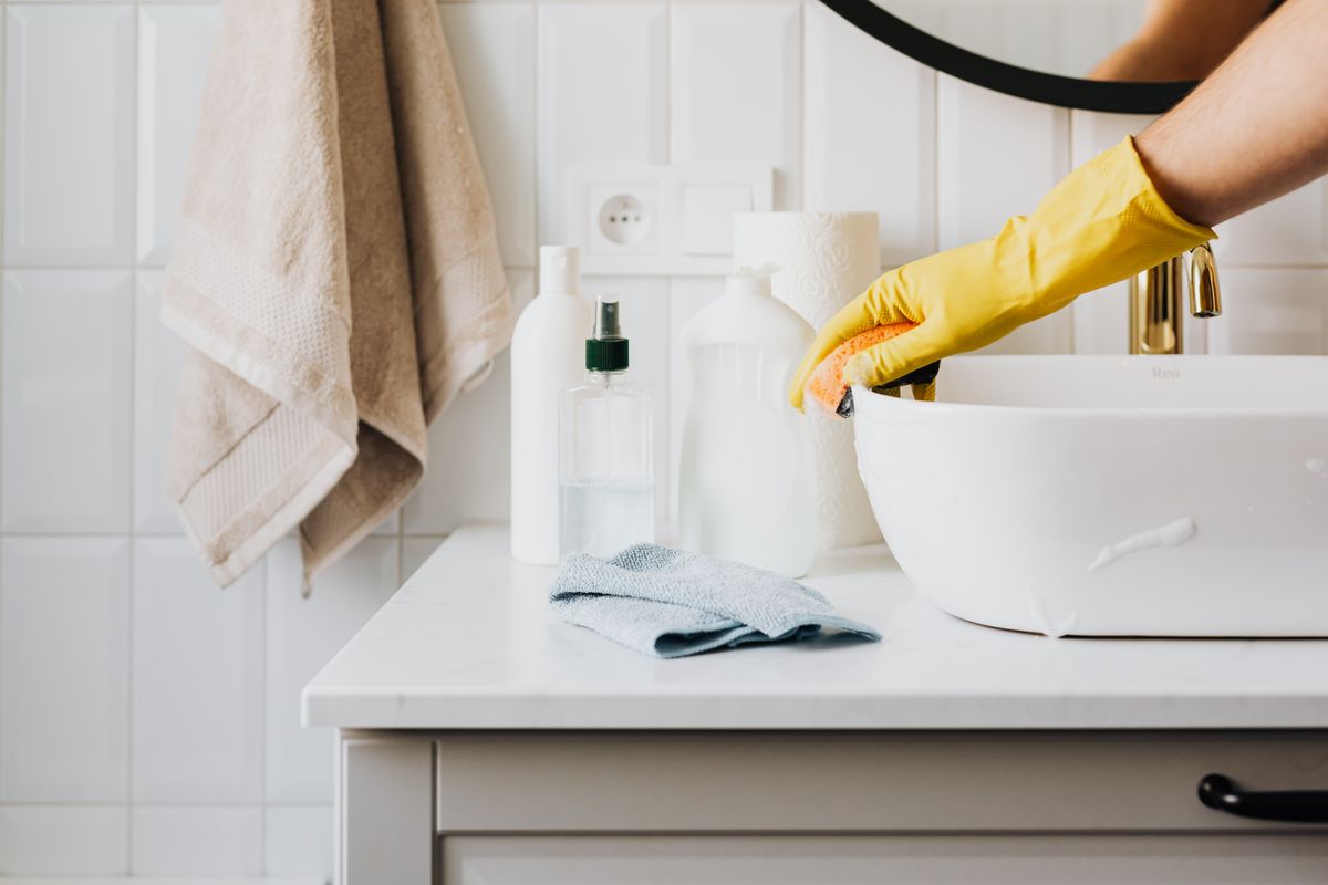 Illustrative photo of a gloved hand cleaning a bathroom basin
